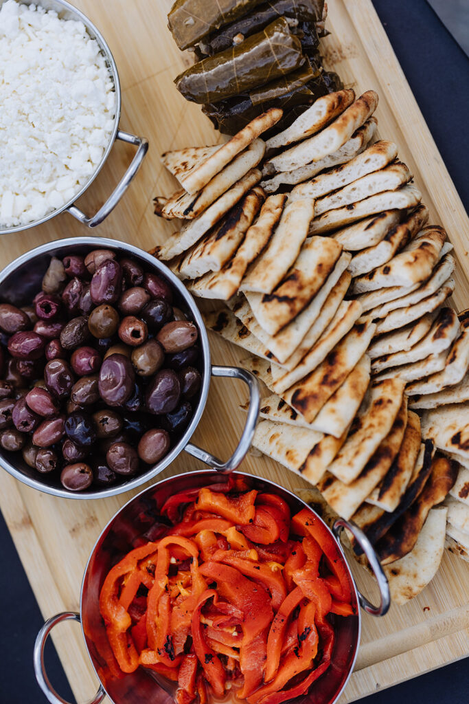 The perfect Mediterranean Party Platter for a cocktail hour with feta cheese, Dolmas, olives, pita bread, and bell pepper on a wooden board