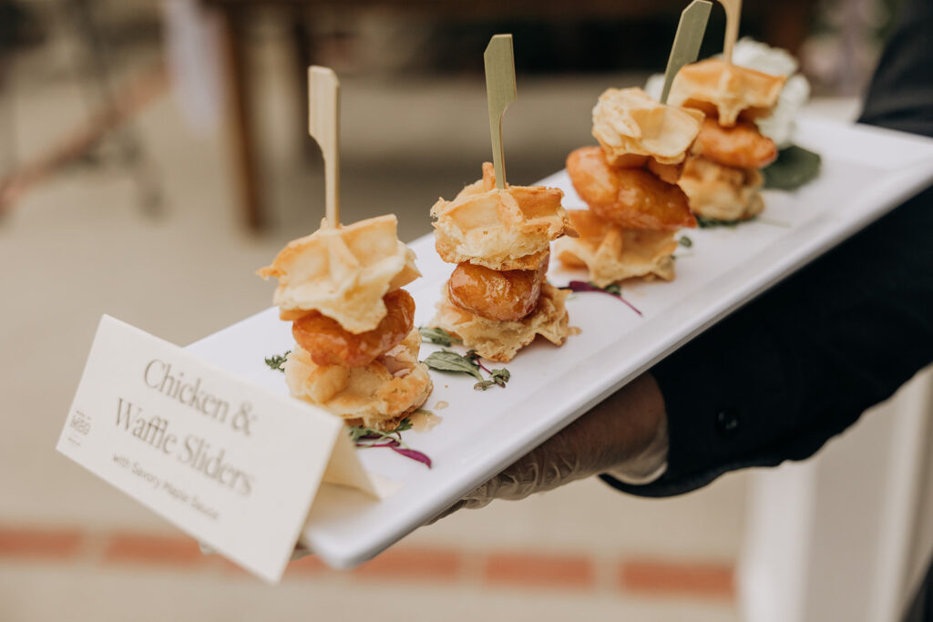 Mini Chicken and Waffle Sandwiches on a White Plate being passed by a server wearing gloves at cocktail hour reception