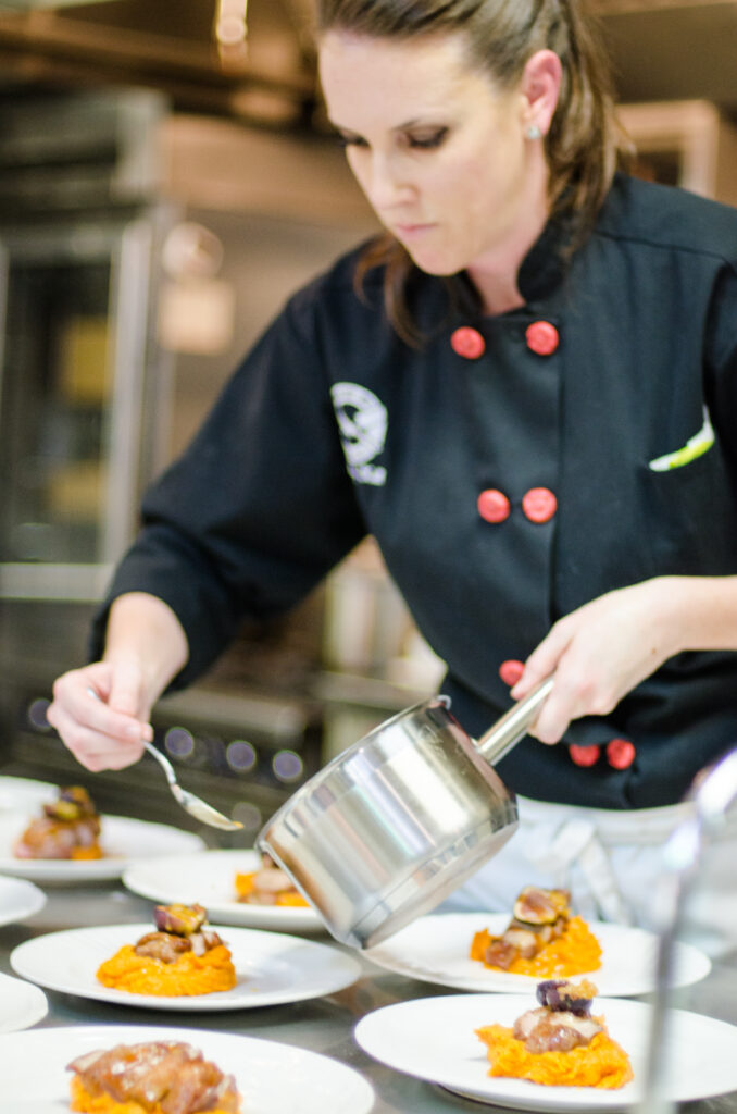 Focused Chef Meg preparing dishes holding a pot in one hand and a spoon in another for an event 