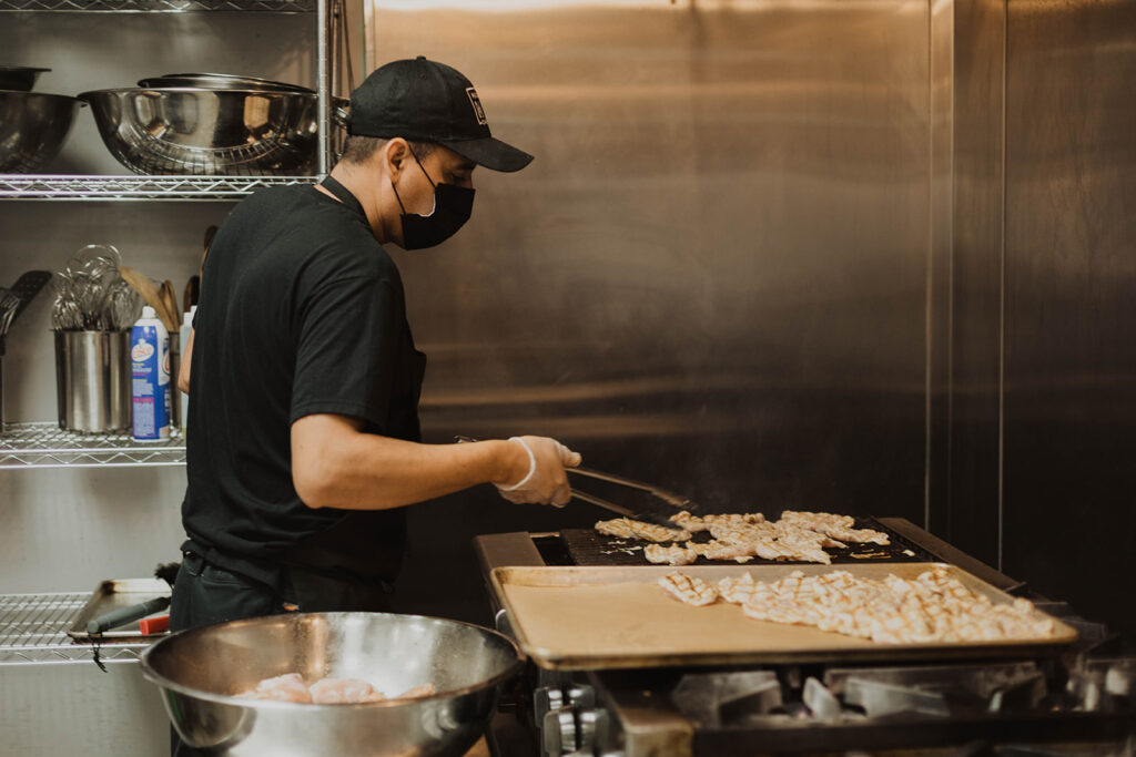 Chef cooking chicken on a grill before transferring to a pan in a industrial kitchen for an event in Southern California