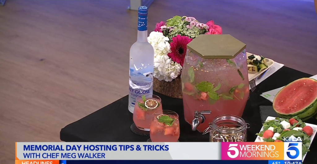 Screenshot of KTLA Memorial Day segment featuring Chef Meg Walker of Made by Meg Catering's pre-batched Watermelon Mint Refresher mocktail in a hexagon glass dispenser with fresh watermelon juice, watermelon chunks (both to go into the dispenser and on the side to go in the glassware), fresh squeezed lime juice, house made mint syrup, fresh mint leaves, and soda water