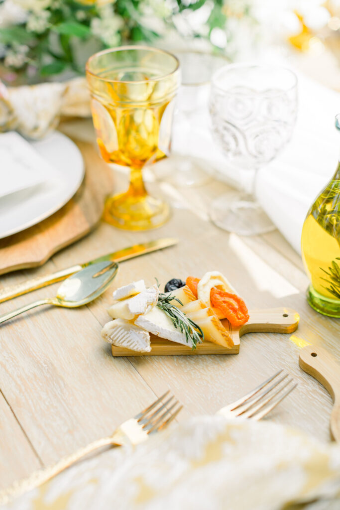 Individual Mini Cheese Board with dried fruit, a variety of cheeses, and fresh rosemary placed on a table among water cups, silverware, plates, and napkins