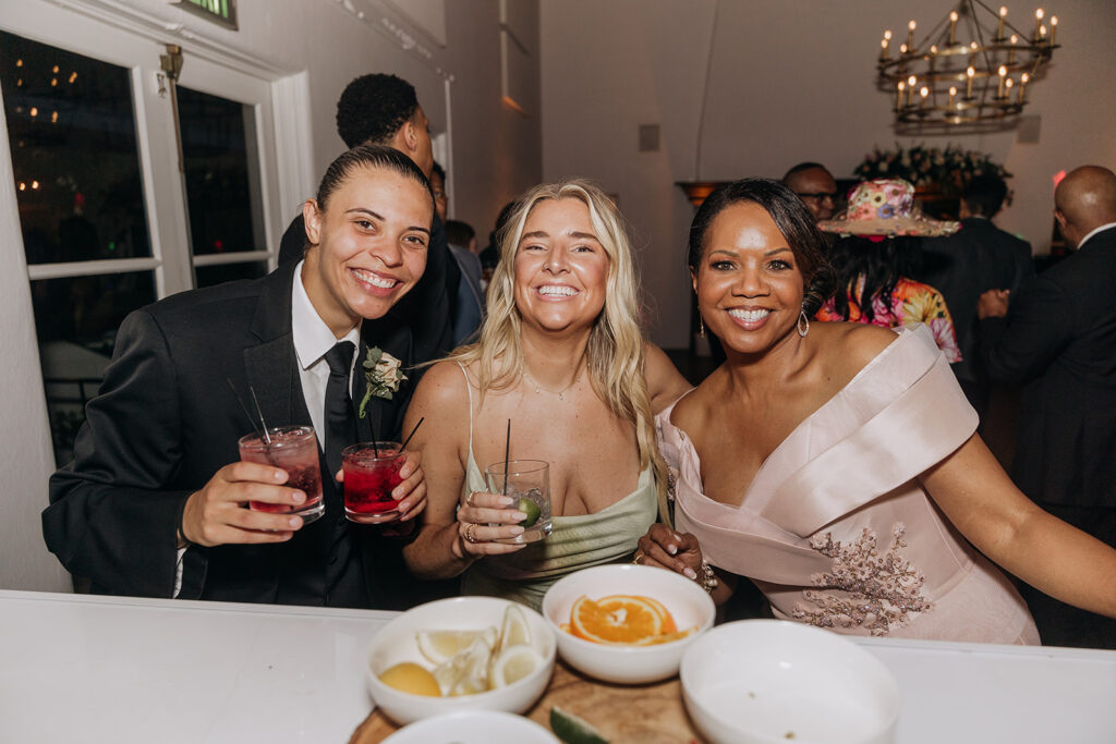 Wedding Bar with Guests Holding Cocktails Next to Garnishes