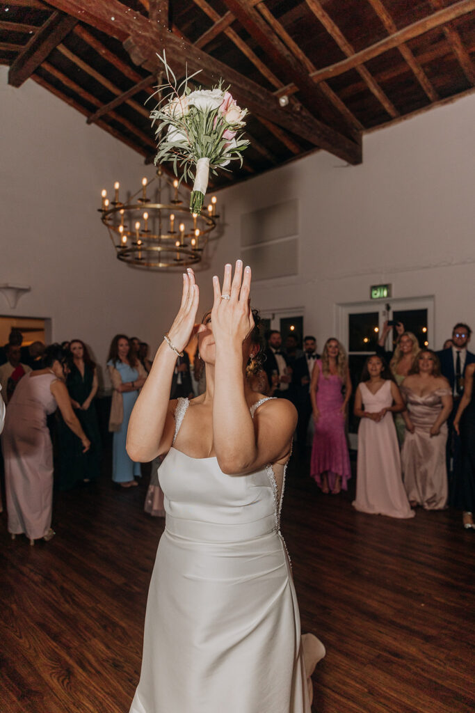 Bride Tosses Bouquet to Group of Single Ladies behind her in the ballroom at La Venta Inn with high ceilings