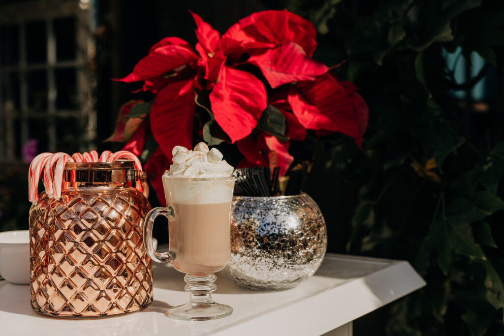 Hot Chocolate in a Glass Hot Cup with Whipped Cream and Marshmallows at the Beverage Station at La Venta Inn in Palos Verdes with a red poinsettia on the bar and a copper container with candy canes, all in natural sunlight outside