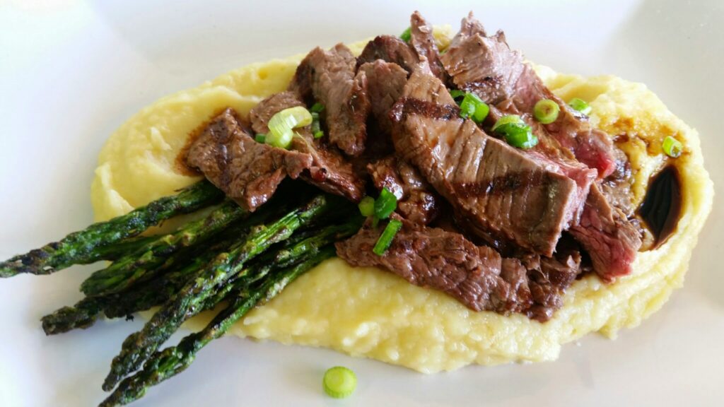 Close up angle of a steak dish with peas, mashed potatoes and grilled asparagus.