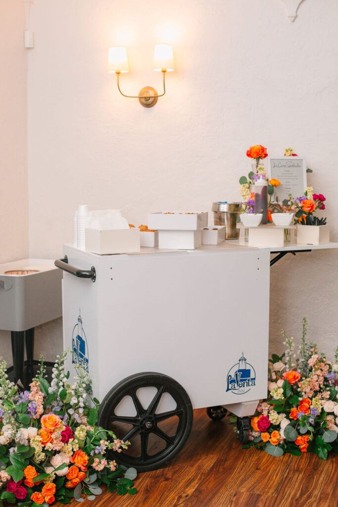 Candid shot of a white ice cream cart surrounded by several colorful bouquet arrangements.