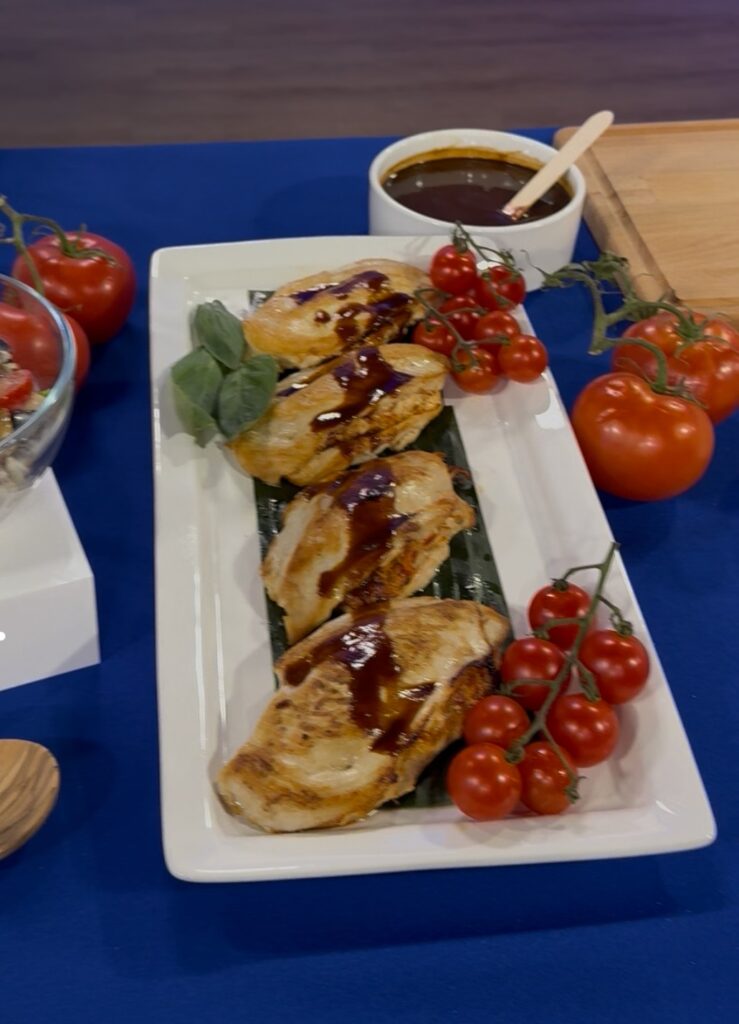 Another photo of the stuffed chicken breast on a tray pass plate. The plate consists of 4 stuffed chicken breasts on a banana leaf with basil and tomatoes on the vine.  Around the plate is a larger bowl of the marsala wine sauce and cherry tomatoes on the vine.